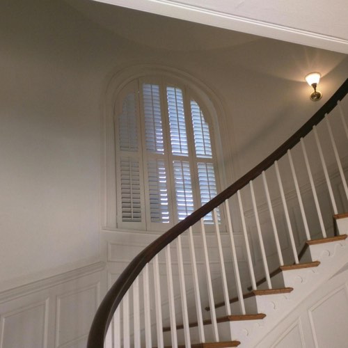 White plantation shutters adorning rounded window located in round stairwell.